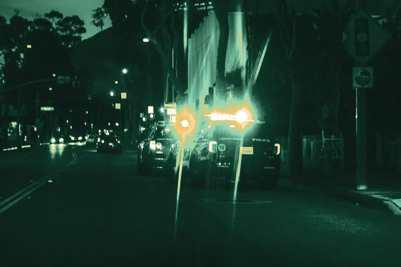 Police cars with flashing lights stopped at the curb of a city street at dusk