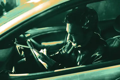 Driver sitting in a parked car at night, writing notes in a small notebook